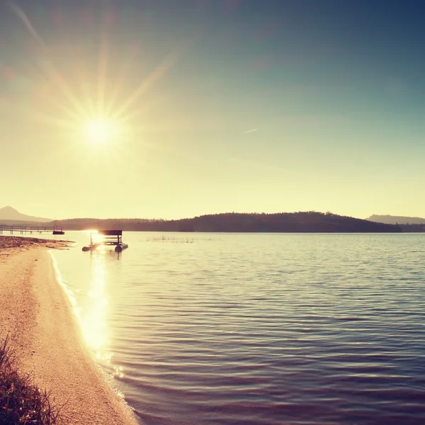 Verlassenes altes rostiges Tretboot, das im Sand des Strandes feststeckt. Welliger Wasserspiegel, Insel am Horizont. — Stockfoto