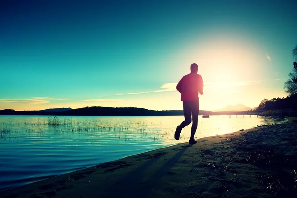 Silhouette av sportslig aktiv mann som løper og trener på stranden ved solnedgang . – stockfoto