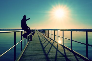 Adam iskele üzerinde oturup sabah denize tadını çıkarın. Güneşli açık mavi gökyüzü, yumuşak su seviyesi