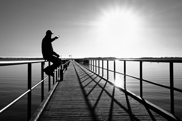 Homme assis sur le quai et profiter de la matinée en mer. Ciel bleu clair ensoleillé, niveau d'eau lisse — Photo