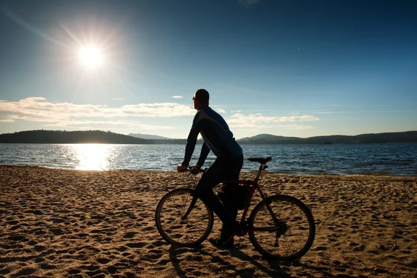 Jovem ciclista silhueta no céu azul e pôr do sol de fundo na praia. Fim de estação no lago . — Fotografia de Stock
