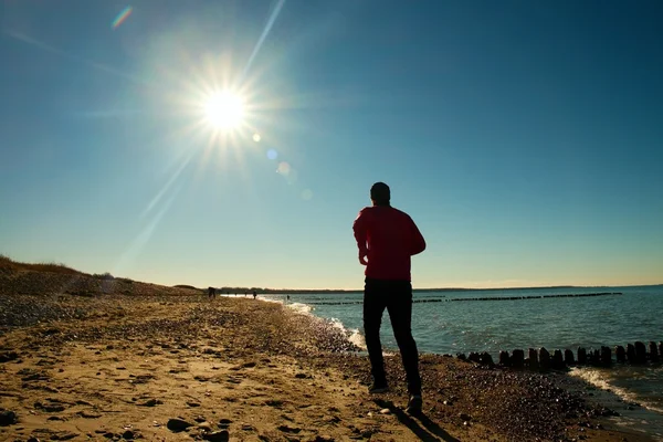 Großer Mann in dunkler Sportkleidung, der am steinigen Strand an der Buhne läuft und trainiert. lebhafte und vignettierende Wirkung — Stockfoto