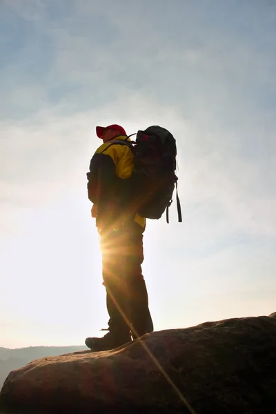 Silhouette of tourist with red cap and  poles in hand. Hiker with big backpack stand on rock. Sunny spring daybreak in rocky mountains. — Stock Photo, Image