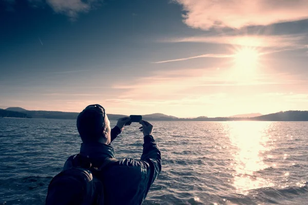 Vysoká nazrzlé vlasy člověka turistické fotografie nebo video s telefonem. Podzimní slunný den na moři — Stock fotografie