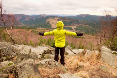 Sarı sıcak ceketli çocuk bir kayada bir soğuk rüzgarlı bahar günde hazır. Aktif yaşam tarzı, açık hava etkinlikleri, yürüyüş