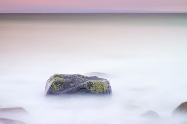Denizde romantik atmosferi huzurlu sabah. Büyük kayalar pürüzsüz dalgalı denizden çıkmış. Pembe ufuk