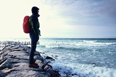 Sahilde sportif sırt çantası ile koyu spor giyim, ufuk bulutlar ile mavi gökyüzü ile uzun uzun yürüyüşe çıkan kimse. 