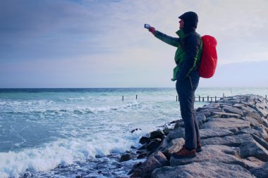 Fiyatı iskelesi fotoğraf sabah deniz üzerinde. Turist ile akıllı telefon elinde, kırmızı yağmurluk sırt çantalı. Harika sabah 