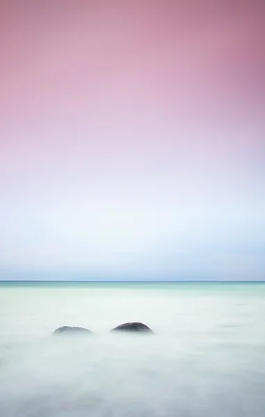 Romantic atmosphere in peaceful morning at sea. Big boulders sticking out from smooth wavy sea. Pink horizon — Stock Photo, Image