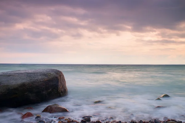 在安静的早晨在海上的浪漫气氛。从平静的波浪大海中伸出的巨砾。粉红色的地平线 — 图库照片