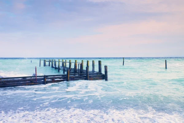 Abandoned wooden wharf in sea within sunrise.Gentle blue pink color of sky, blur waves