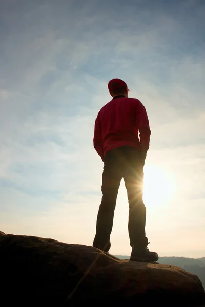 Caminante en sudadera roja con gorra roja en pico de roca vigilando valle a sol. Hermoso momento — Foto de Stock