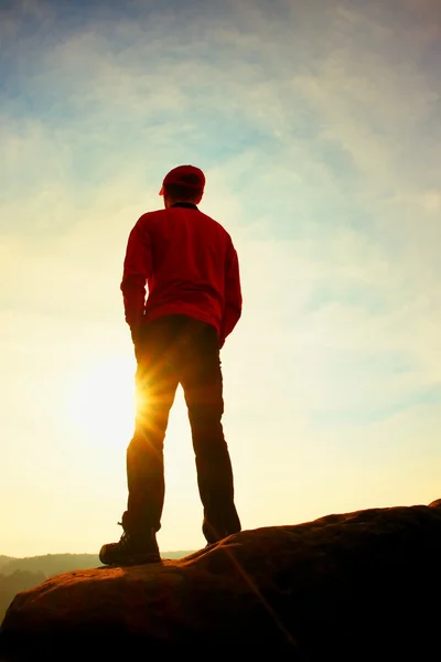 Caminante en sudadera roja con gorra roja en pico de roca vigilando valle a sol. Hermoso momento — Foto de Stock