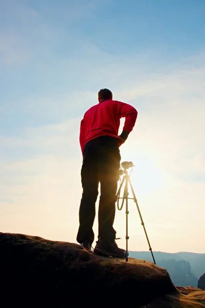 Professionell fotograf tar bilder med kameran på stativ på rocky peak. Drömmande våren landskap. — Stockfoto