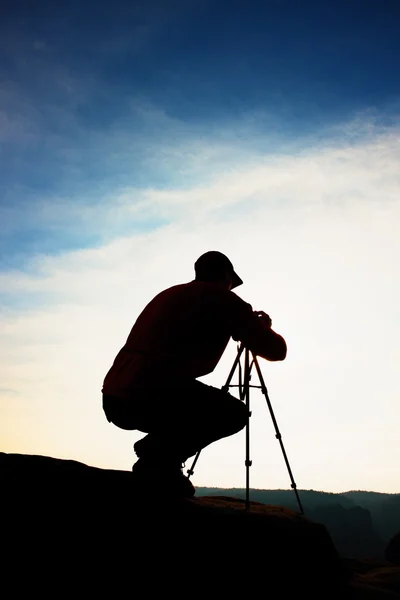 Professional photographer takes photos with camera on tripod on rocky peak. Dreamy spring landscape. — Stock Photo, Image