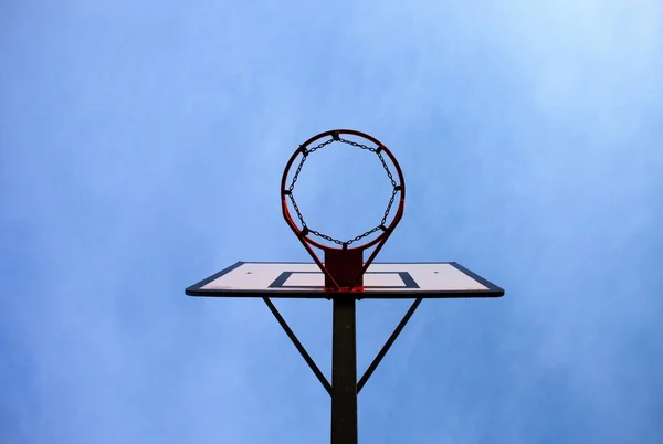 Antiguo tablero de baloncesto descuidado con aro oxidado sobre la cancha de la calle. Cielo azul — Foto de Stock