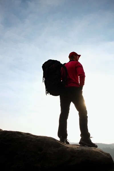 Einsamer Tourist mit großem Rucksack steht auf Felswand und blickt in tiefes Tal. — Stockfoto