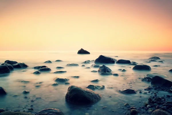 Romantische ochtend op zee. Grote keien van gladde water niveau uitsteken. Roze horozon met de eerste warme zonnestralen. — Stockfoto