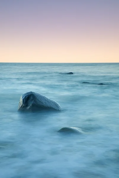Ρομαντική ατμόσφαιρα σε ήσυχη το πρωί στη θάλασσα. Μεγάλες πέτρες να κολλήσει έξω από την ομαλή, κυματιστό θάλασσα. Ροζ ορίζοντα — Φωτογραφία Αρχείου