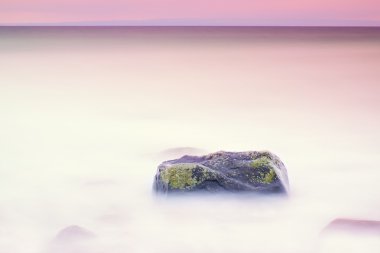 Denizde romantik atmosferi huzurlu sabah. Büyük kayalar pürüzsüz dalgalı denizden çıkmış. Pembe ufuk