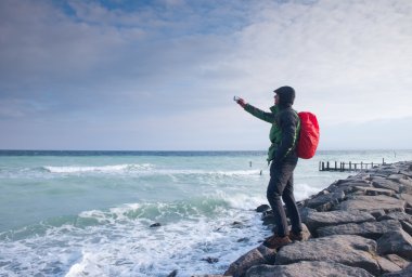 Fiyatı iskelesi fotoğraf sabah deniz üzerinde. Turist ile akıllı telefon elinde, kırmızı yağmurluk sırt çantalı. Harika sabah 