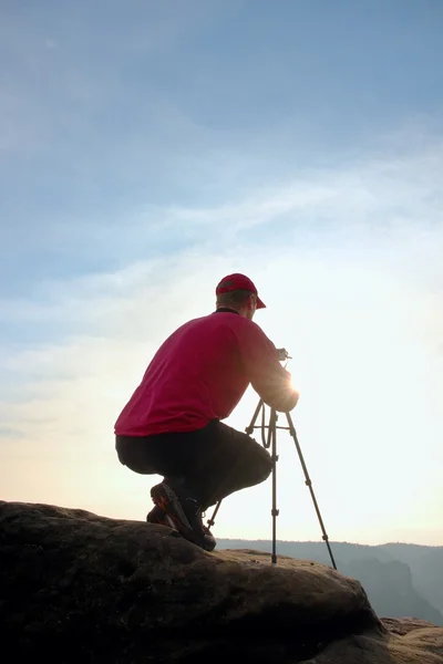 Photographerin röd jacka och röd keps bo med kamera på stativ på klippan och tänkande. Drömska landskap. — Stockfoto