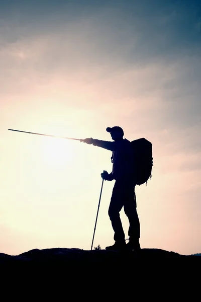 Tourist guide show the right way with pole in hand. Hiker with sporty backpack stand on rocky view point above misty valley. — Stock Photo, Image