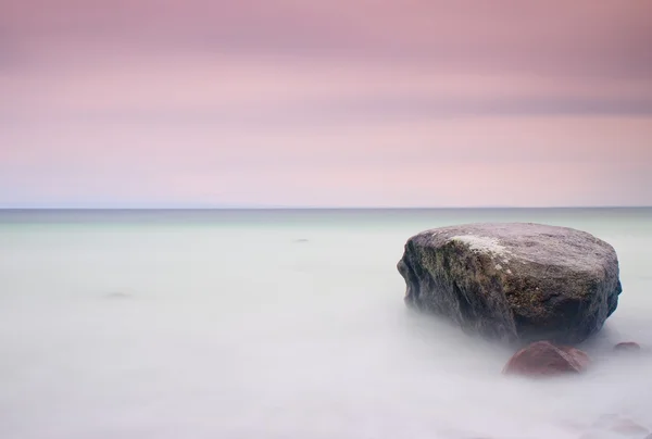 Ambiente romántico en la mañana tranquila en el mar. Grandes rocas que sobresalen del suave mar ondulado. Horizonte rosa — Foto de Stock