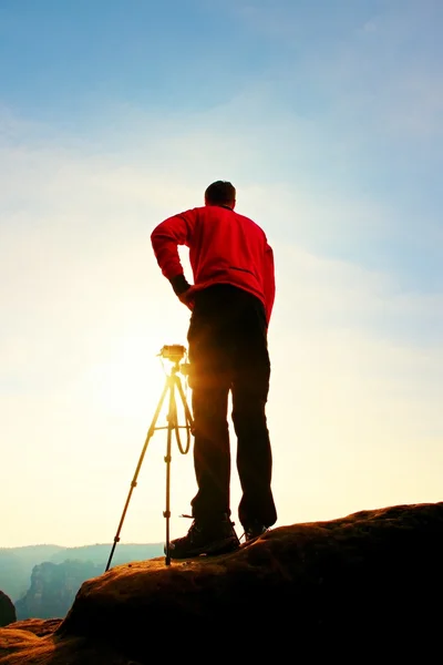 Fotógrafo profissional tira fotos com câmera no tripé no pico rochoso. Paisagem de primavera sonhadora . — Fotografia de Stock