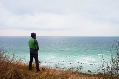 Yeşil windcheater adam cliff bay ve deniz kadar ufuktan looki yukarıda durmak.