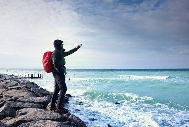 Fiyatı iskelesi fotoğraf sabah deniz üzerinde. Turist ile akıllı telefon elinde, kırmızı yağmurluk sırt çantalı. Harika sabah 