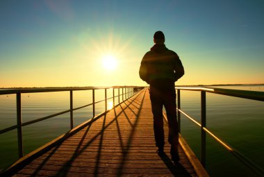 Adam siluet yürüyüş güneş fantastik sabah denize yukarıda iskele inşaatı.