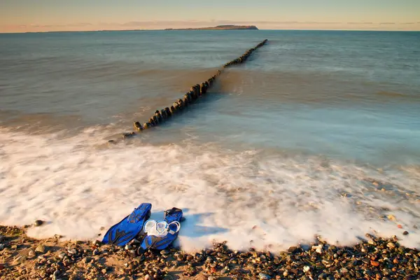 Mascarilla con aletas azules para snorkel lista para usar en playa pedregosa en rompeolas . —  Fotos de Stock