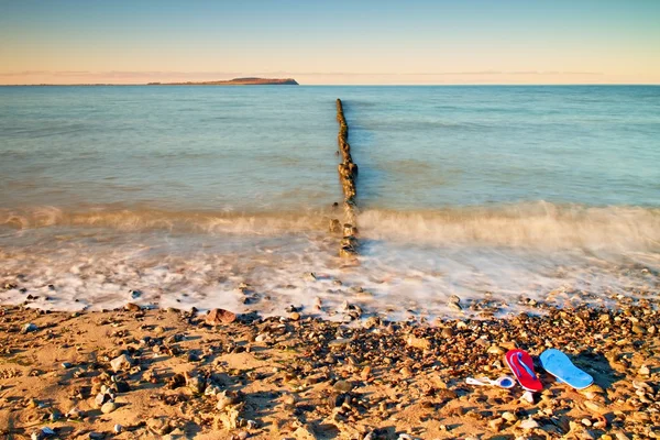 Blauw rood Flip Flops en witte Zwemmen goggles klaar voor het gebruik op stenige strand van houten golfbreker. — Stockfoto