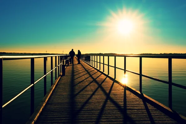 Mattina in porto. I turisti camminano sul molo sopra il mare. Cielo azzurro chiaro, livello dell'acqua liscio — Foto Stock