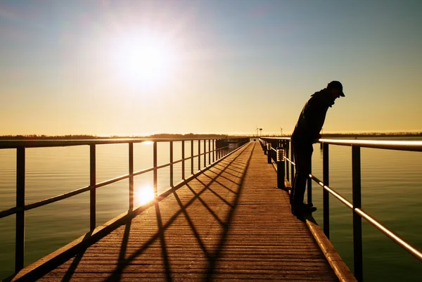 Un hombre solo en el muelle y mirar por encima de pasamanos en el agua. Cielo despejado soleado, agua suave —  Fotos de Stock