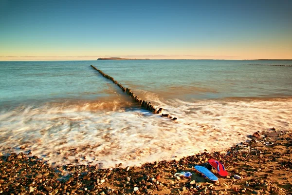 Chinelos vermelhos azuis e óculos de natação brancos prontos para usar na praia pedregosa em quebra-mar de madeira . — Fotografia de Stock
