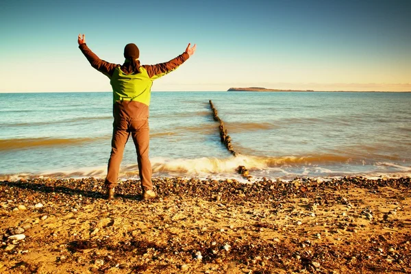 Tourist in green black clothing with hands in the air along beach. Vivid and strong vignetting effect. Stock Image