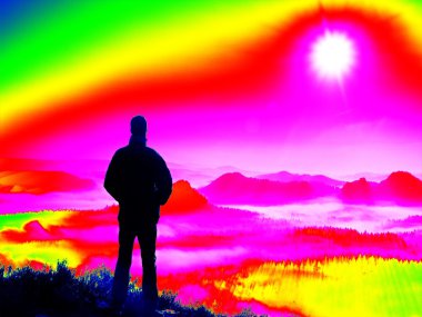 Kızılötesi ölçüm inceden inceye gözden geçirmek. Turist kayalık tepe üzerinde. Dağlarda, ağır turuncu sis harika daybreak