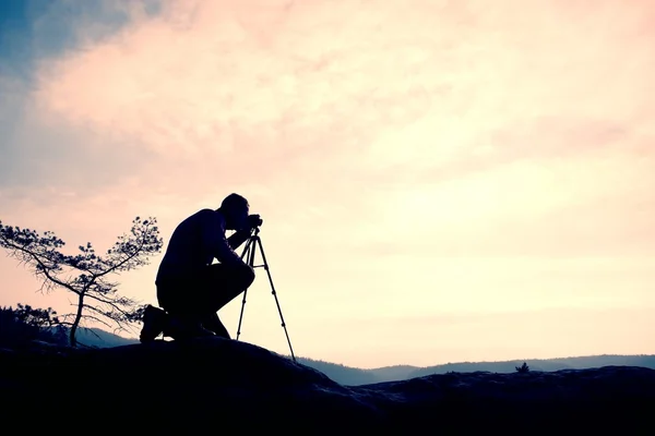 Fotógrafo amador tira fotos com câmera de espelho no pico da rocha. Paisagem nebulosa sonhadora, primavera laranja rosa nebuloso nascer do sol — Fotografia de Stock