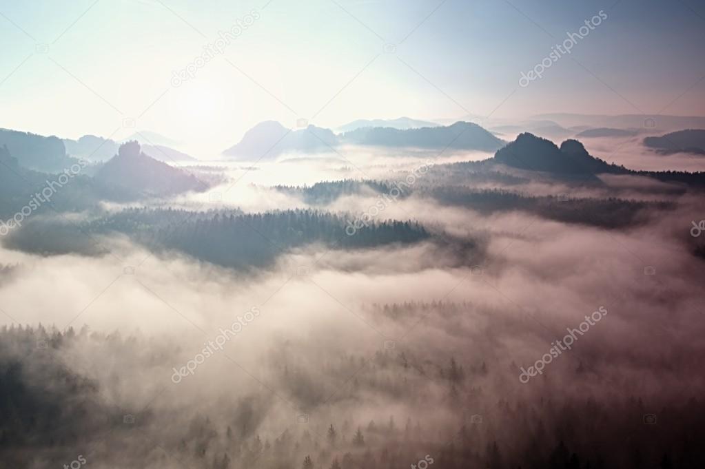 Fantastic dreamy sunrise on the top of the rocky mountain with the view into misty valley