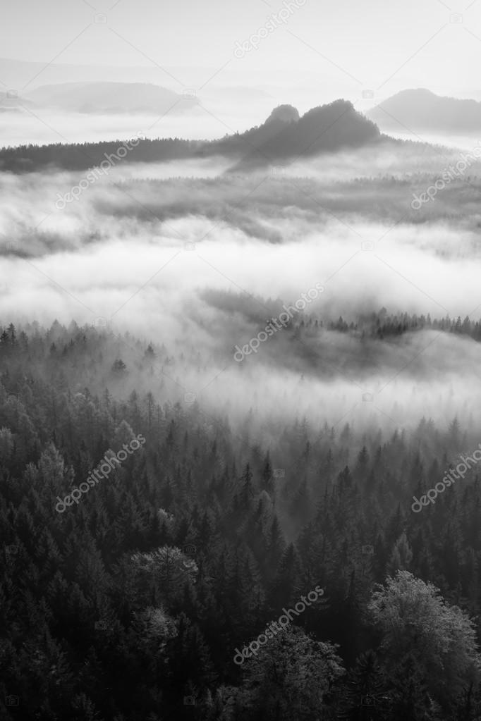 Fantastic sunrise on the top of the rocky mountain with view into misty valley. Black and white 