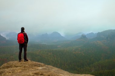 Kaya empires parkta keskin kumtaşı kaya üzerinde kırmızı sırt çantası ile Hiker ve sisli ve sisli bahar vadisinde izliyor