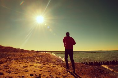 Uzun boylu adam çalıştıran ve dalgakıran, taşlı plajda egzersiz karanlık sportswer. Canlı ve vinyet etkisi