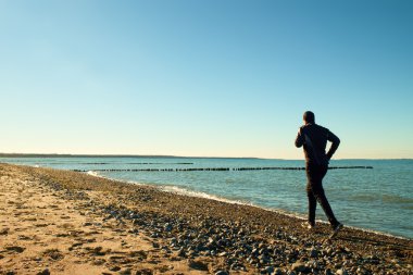Uzun boylu adam çalıştıran ve dalgakıran, taşlı plajda egzersiz karanlık sportswer.
