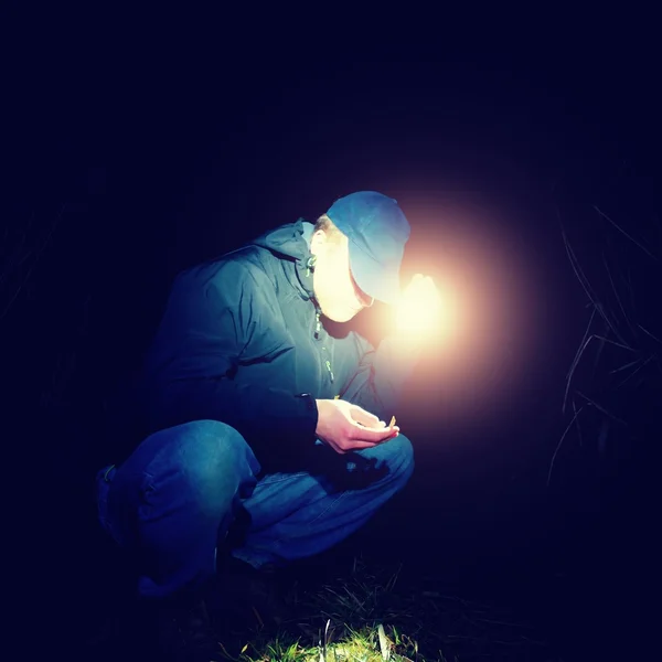 Hombre de azul vistiendo buscando algo en hierba mojada con luz en la mano, noche de miedo o cuento de hadas — Foto de Stock