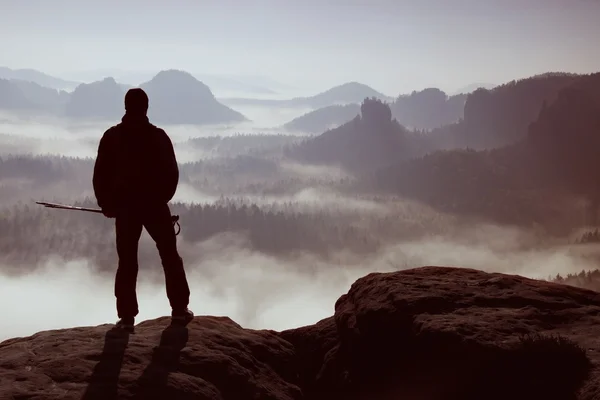 Journée agitée dans les montagnes rocheuses. Silhouette de touriste avec poteaux à la main. Randonneur debout sur le point de vue rocheux au-dessus de la vallée brumeuse . — Photo