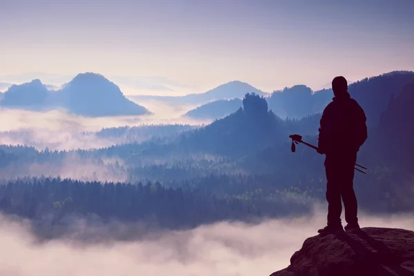 Silueta de turista con bastones en la mano. Amanecer soleado de primavera en montañas rocosas. Caminante con mochila deportiva de pie en el punto de vista rocoso por encima del valle brumoso . —  Fotos de Stock