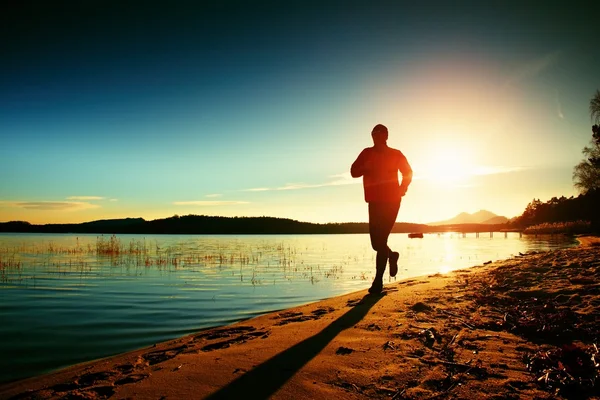 Silhueta de esporte homem ativo correndo e se exercitando na praia ao pôr do sol . — Fotografia de Stock