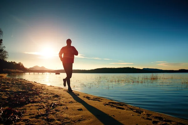 Silhouet van sport actieve man uitgevoerd en uitoefenen op het strand bij zonsondergang. — Stockfoto